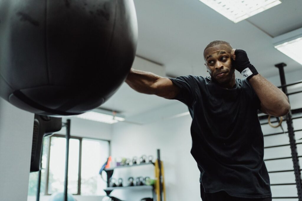 Boxer in black shirt intensely punching a heavy bag during training indoors.