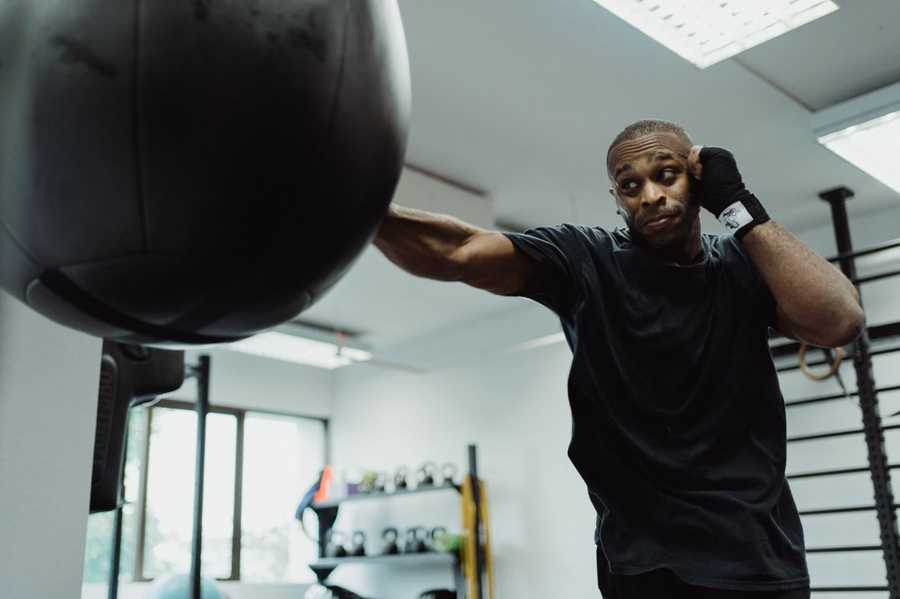 Boxer in black shirt intensely punching a heavy bag during training indoors.